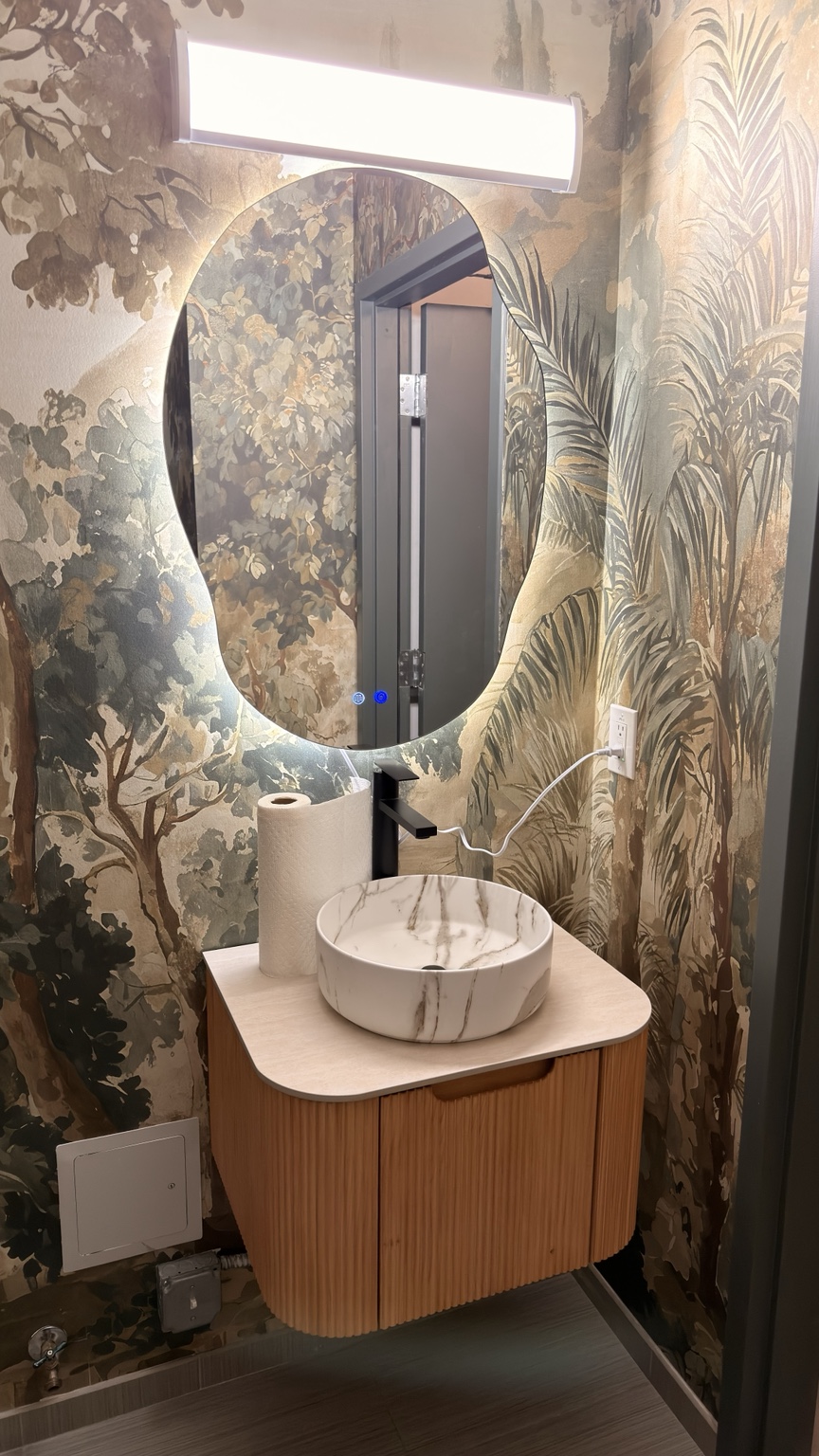 Floating wood vanity with vessel sink and LED mirror against botanical wallpaper