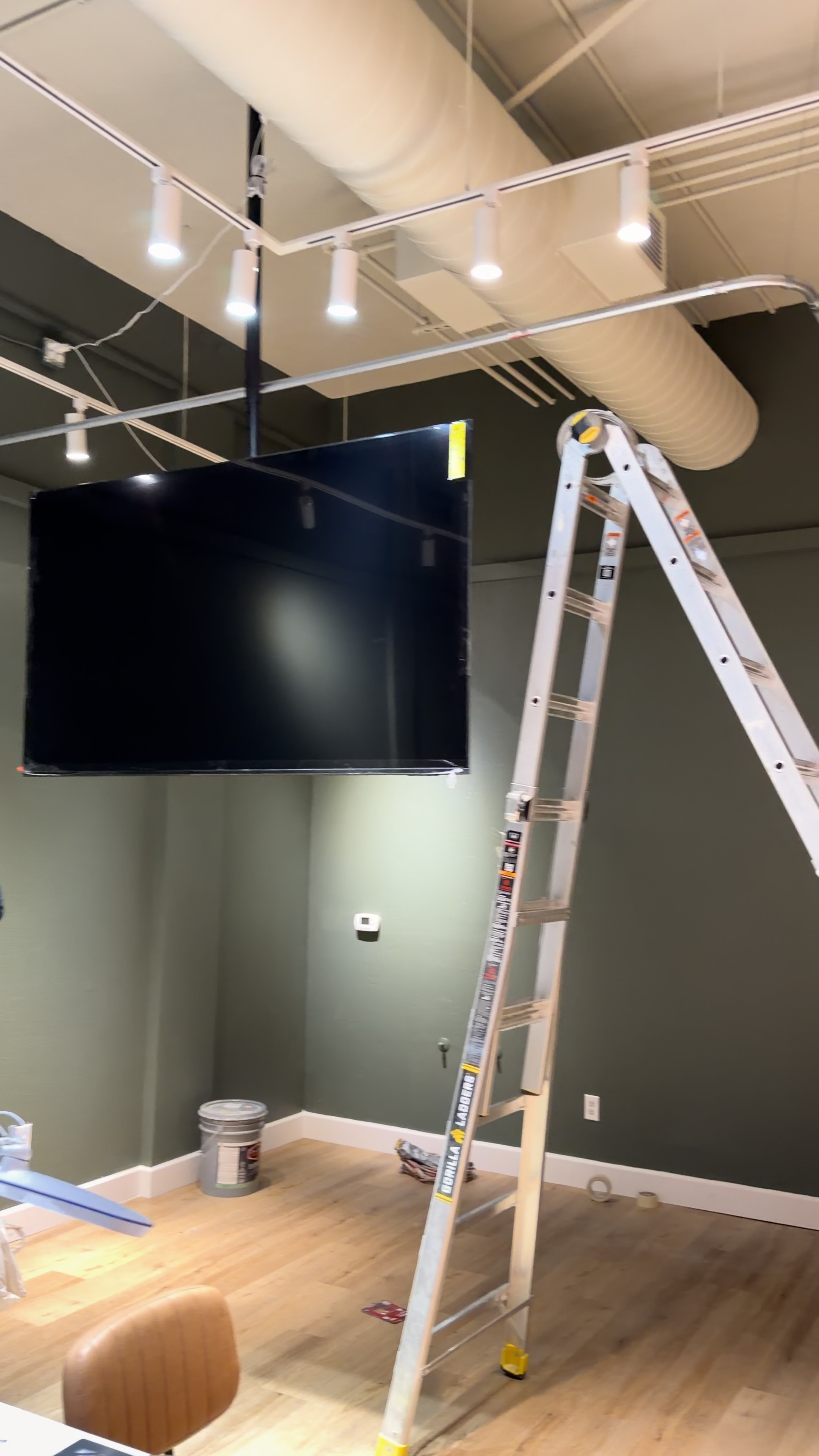 Large television mounted to a black ceiling bracket beside a ladder