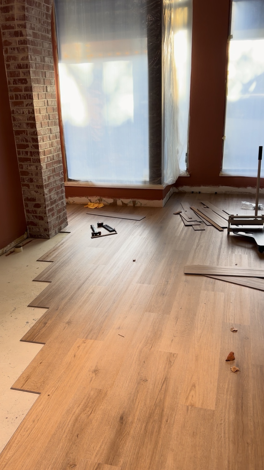 Wood-look flooring installation beside tall windows and a brick column