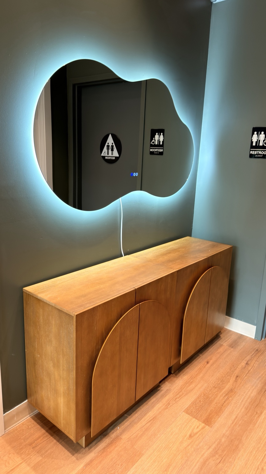 Blue-backlit organic-shaped mirror above two wooden cabinets