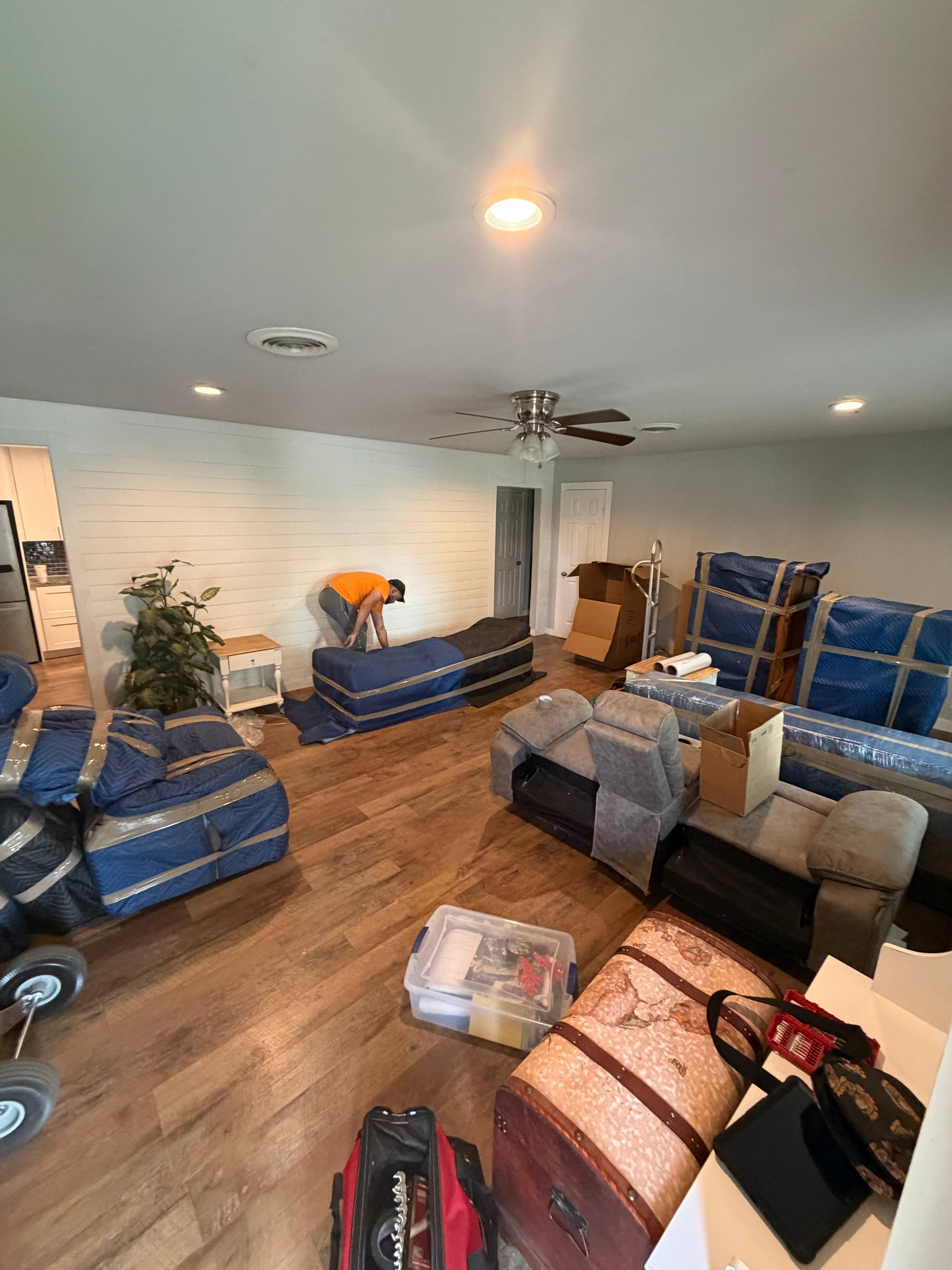 Furniture wrapped in blue moving blankets with packing supplies nearby