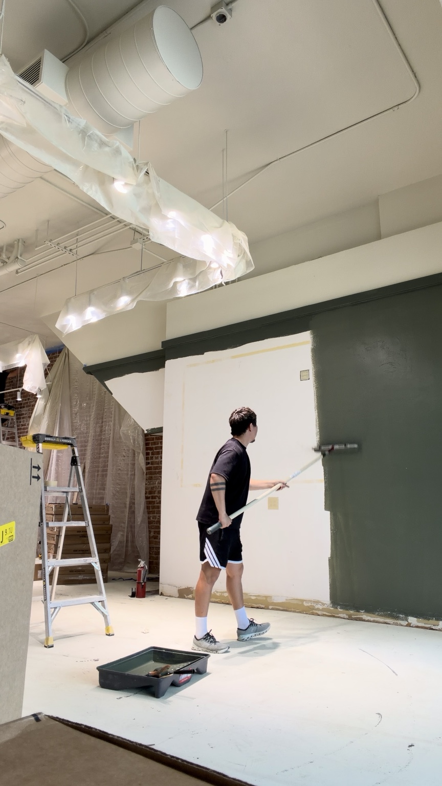 A worker applying green paint to a commercial interior wall