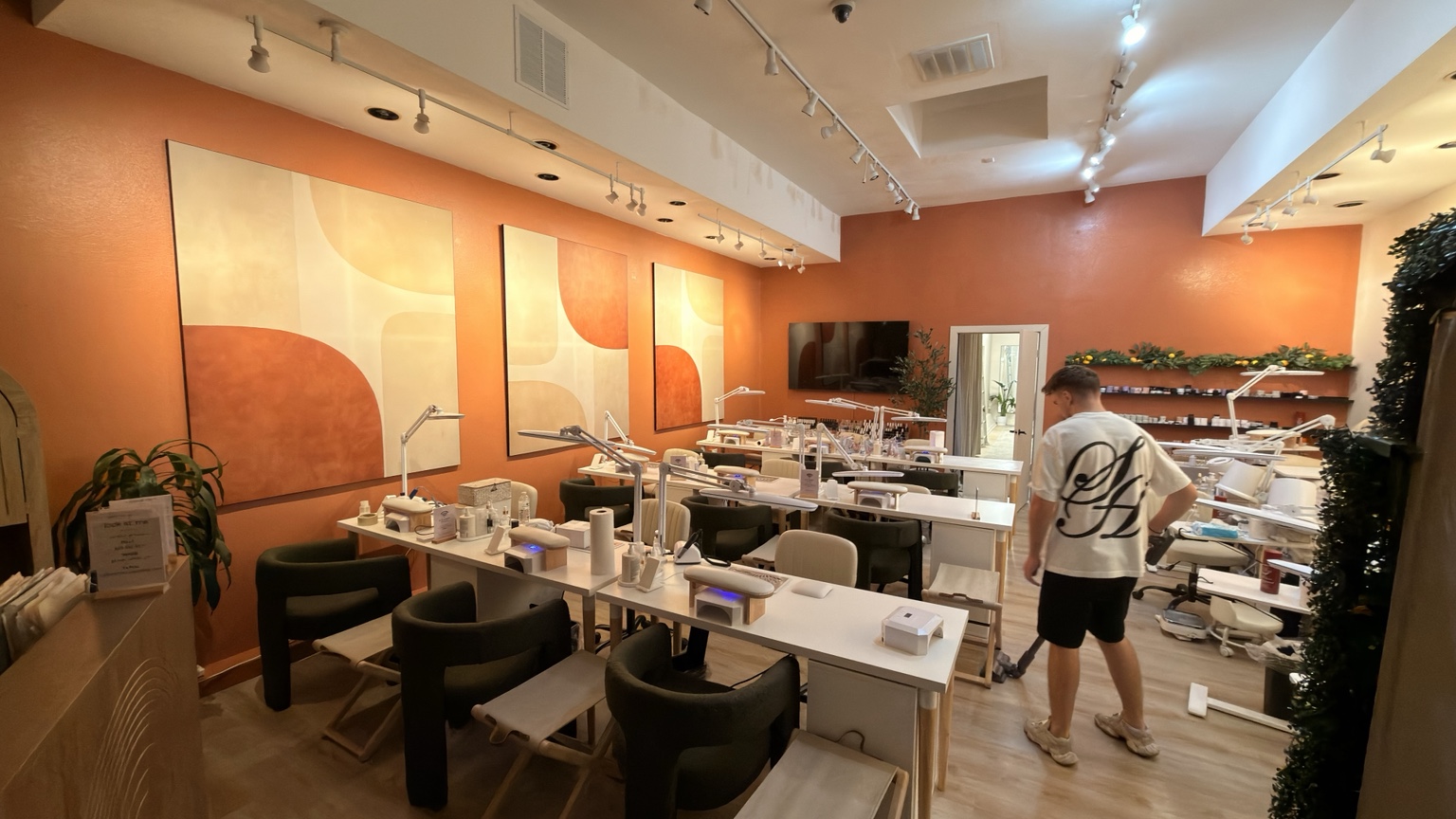 Nail salon with orange walls, large abstract artwork and white workstations
